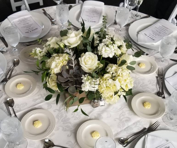 White floral centerpiece with candles on a formal dining table setting