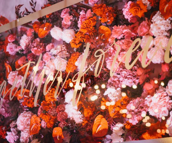 Pink and orange floral wall with cursive white lettering and soft glowing lights