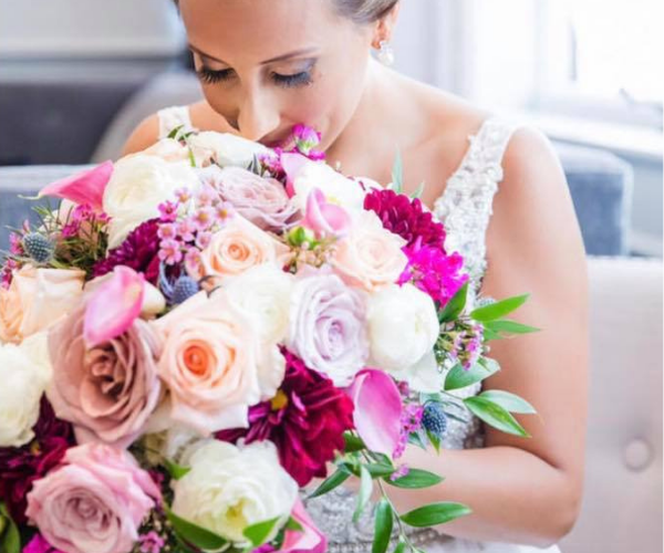 Woman in a white lace dress smelling a large bouquet of pink and white flowers.