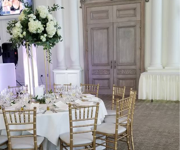 Elegant banquet table with gold chairs and white floral arrangement in a grand hall