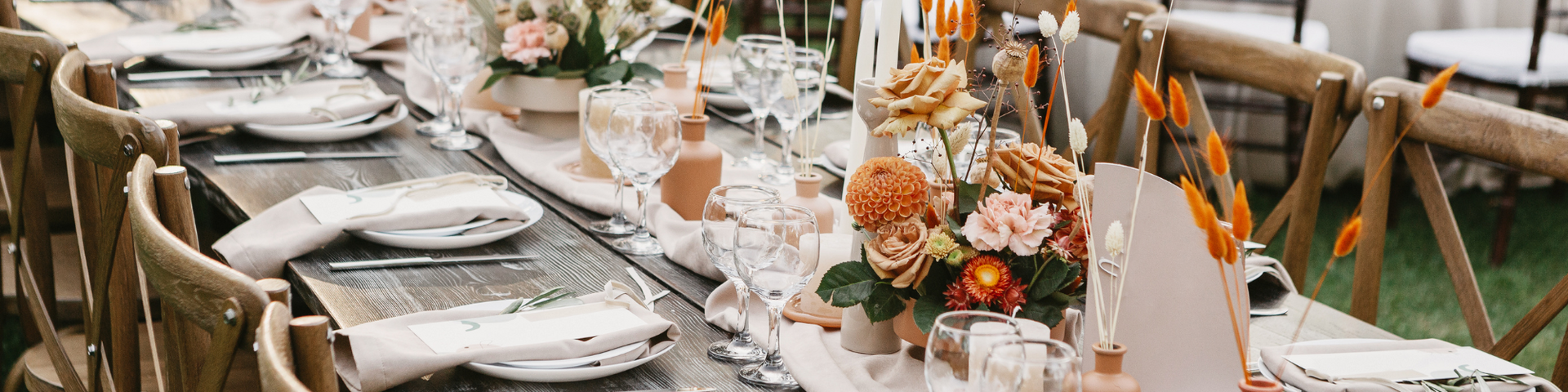 Elegant outdoor dining table set with white plates, floral centerpieces, and wooden chairs on a patio