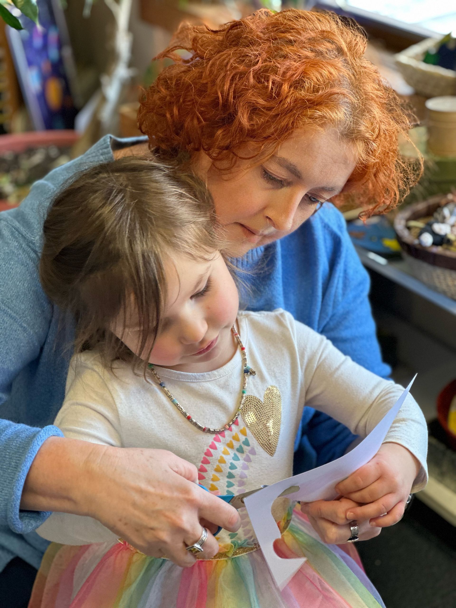 Montessori guide is helping a child cut a piece of paper.