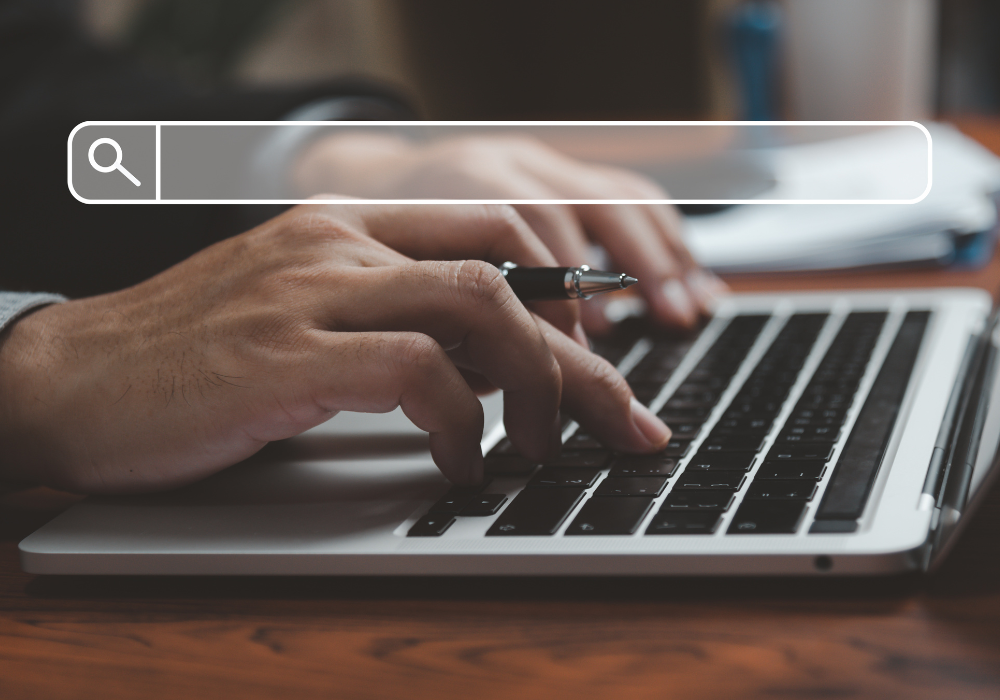 A person is typing on a laptop computer with a pen in their hand.