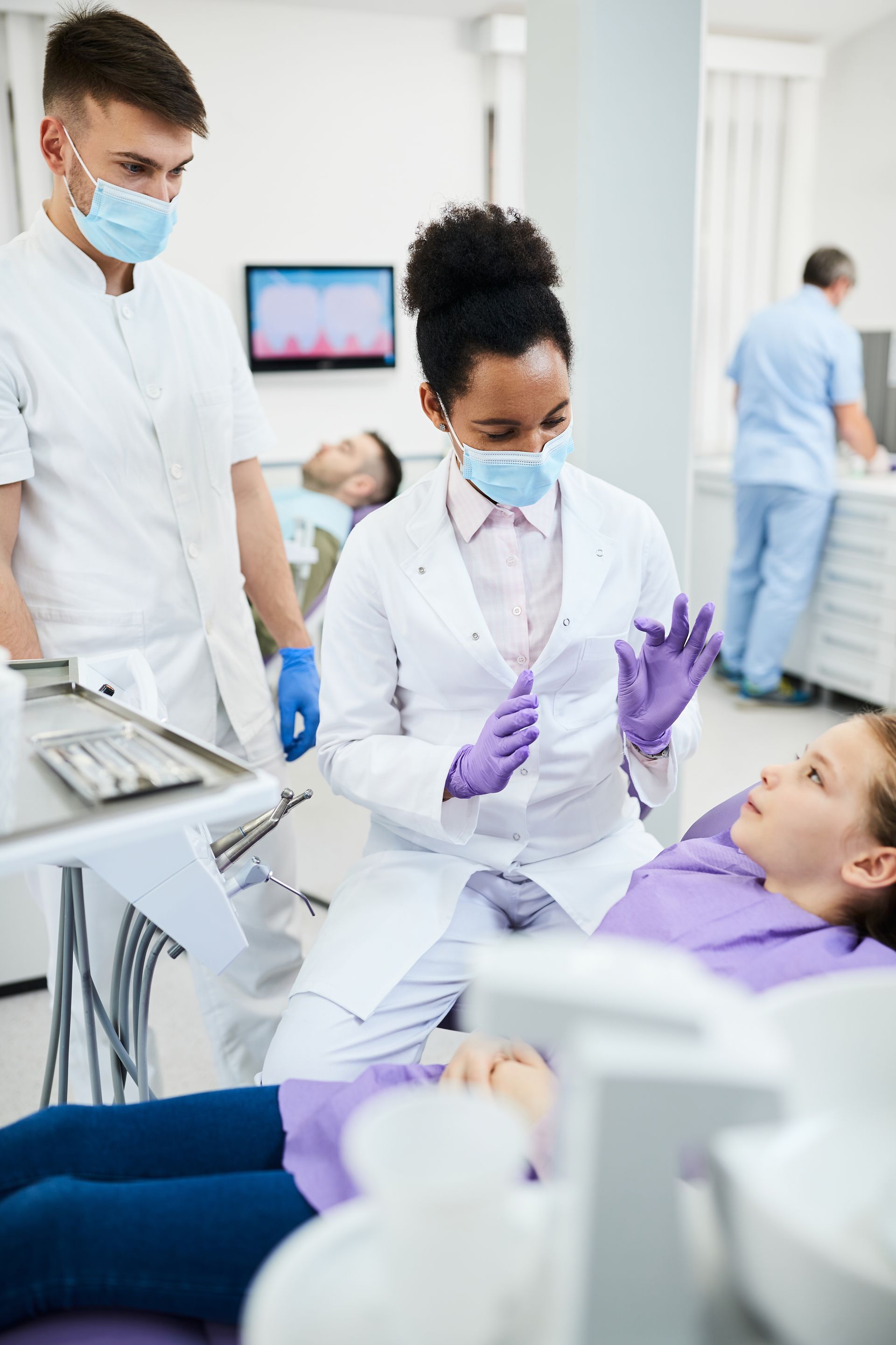 A young girl is sitting in a dental chair while a dentist examines her teeth.