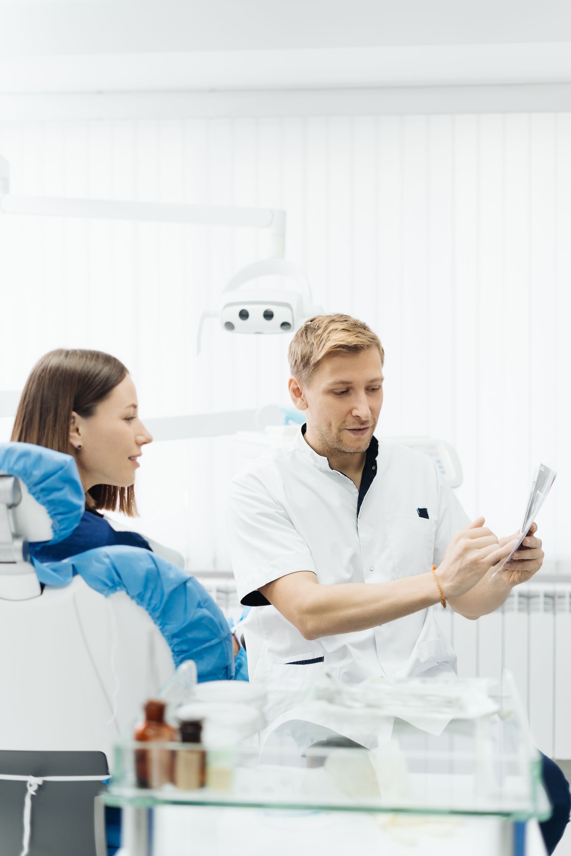 A dentist is talking to a patient in a dental chair while looking at a tablet.