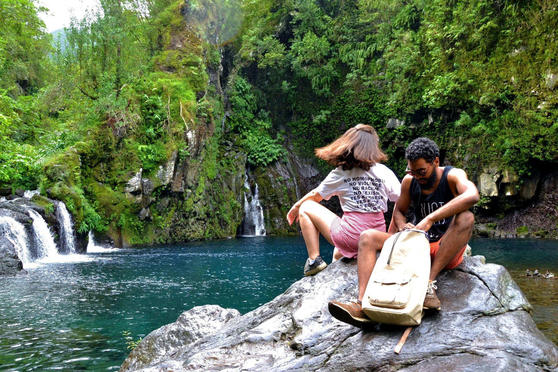 A man and a woman are sitting on a rock near a waterfall.