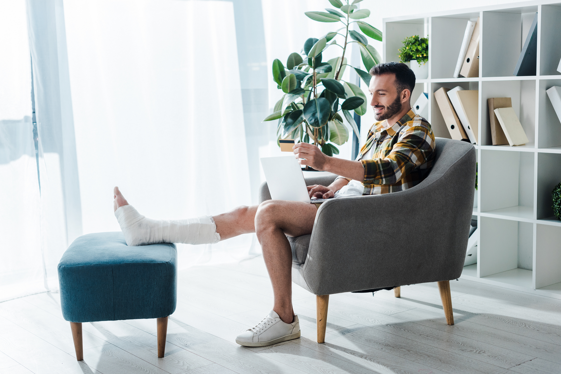 A man with a cast on his leg is sitting in a chair using a laptop computer.