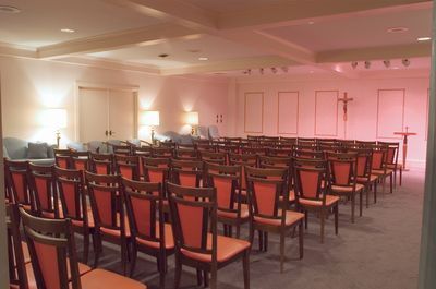 Rows of orange chairs in a light-filled chapel, a cross on the wall, and sofas in the back.