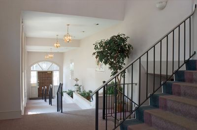 Hallway with staircase, plant, and arched doorway, lit by chandeliers.