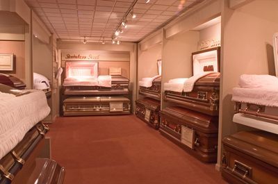 Coffin display room with various caskets arranged on shelves; red carpet, soft lighting.