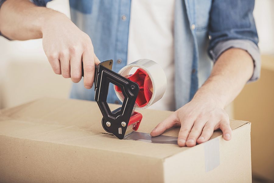 Man sealing moving box with tape dispenser.
