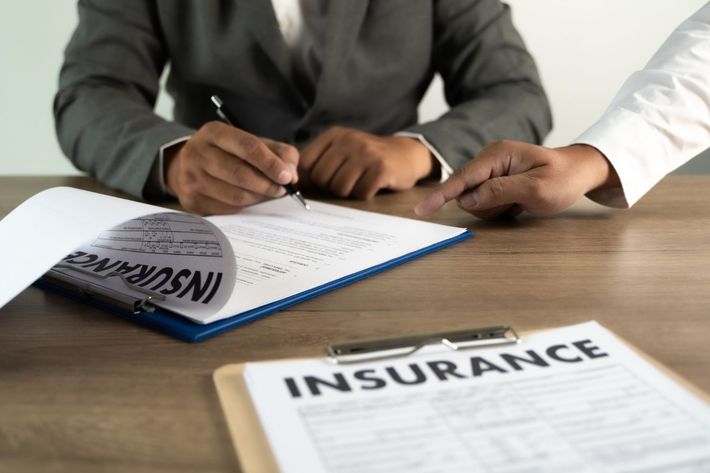 Two people signing an insurance document at a desk with a clipboard and papers