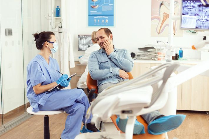 Dentist consulting with seated patient in a bright dental clinic, with an exam chair in the foreground