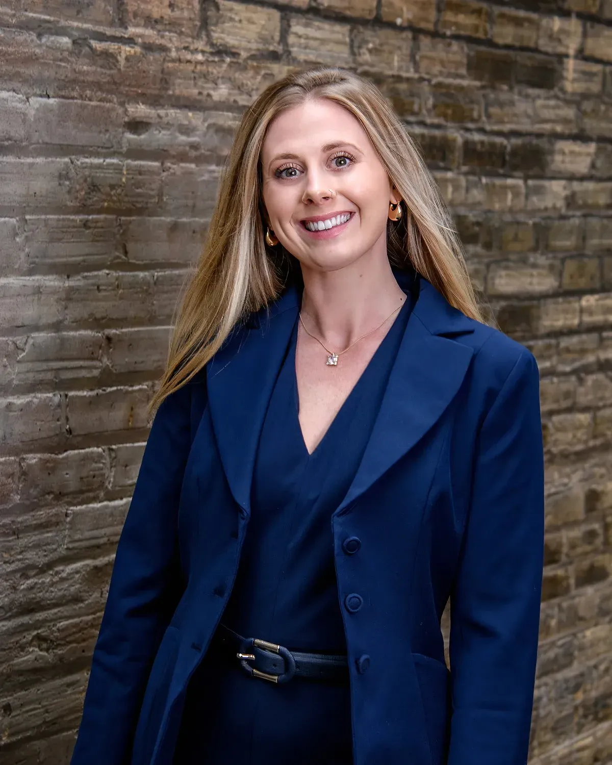 Smiling woman in a navy blazer standing against a brick wall.