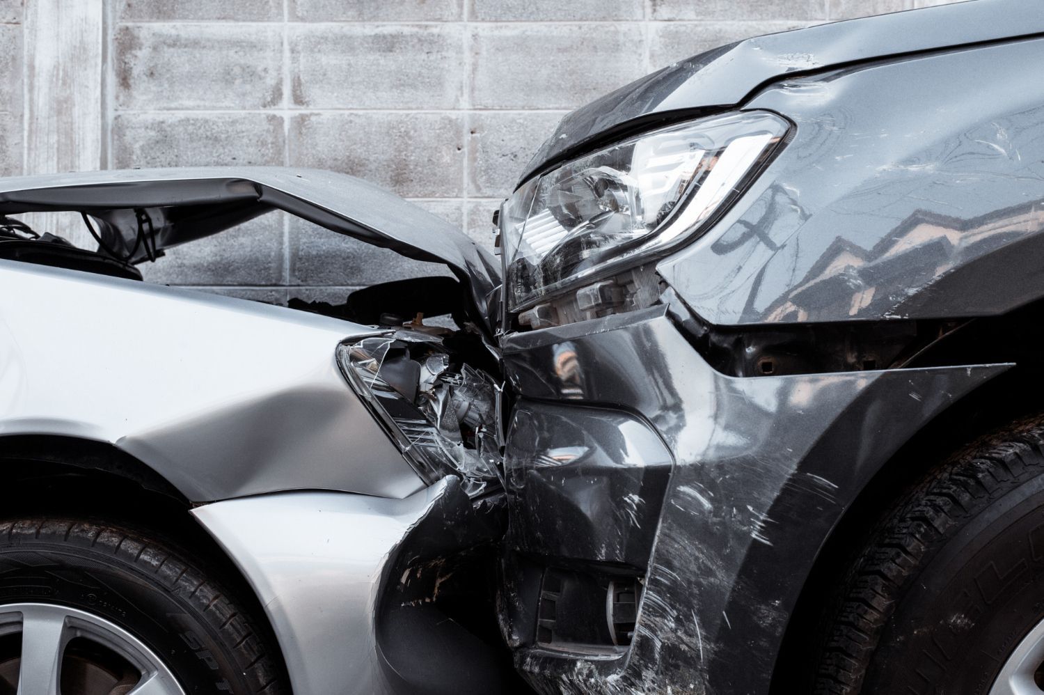 Severe front-end collision between a silver car and a black SUV against a concrete wall
