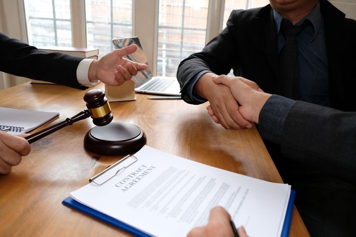 Hands shaking over a contract beside a gavel on a conference table