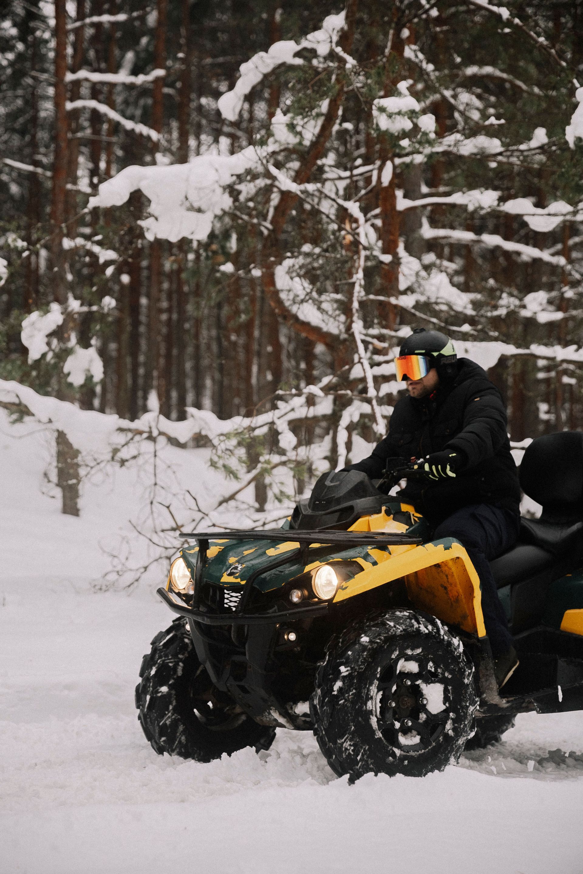 Person riding a yellow ATV through snowy woods