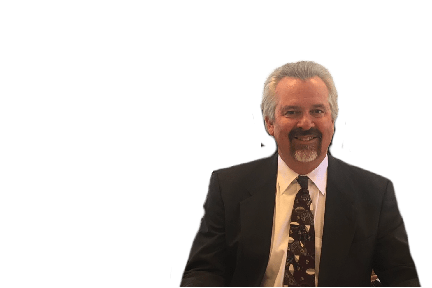Man in a suit smiles. Grey hair, goatee, patterned tie. Against a white background.