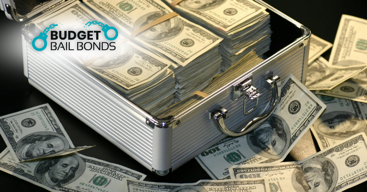 A silver briefcase overflowing with stacks of US one-hundred-dollar bills, with the Budget Bail Bonds logo in the corner.