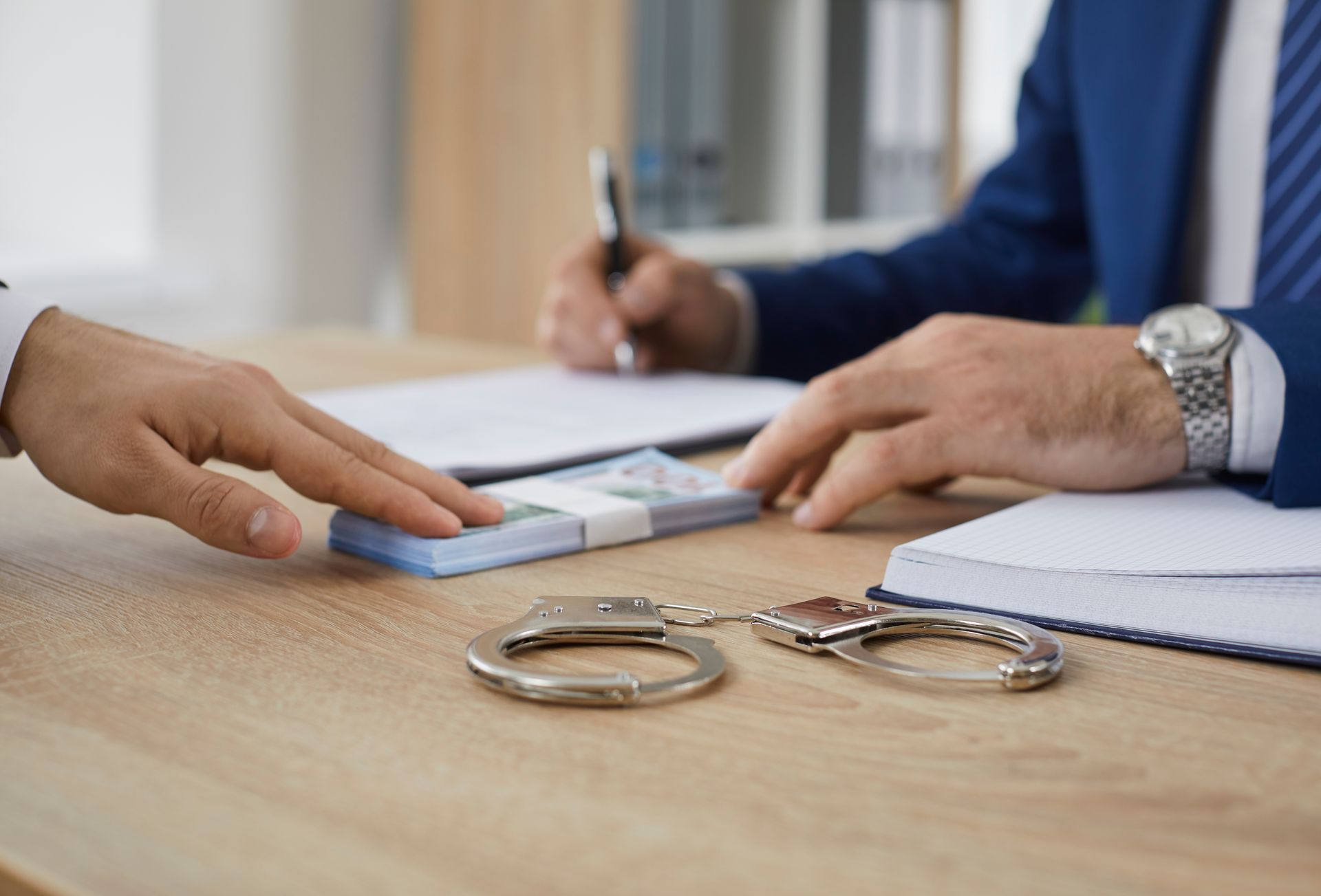 Handcuffs, money, and hands reach for documents on a desk; a person signs.