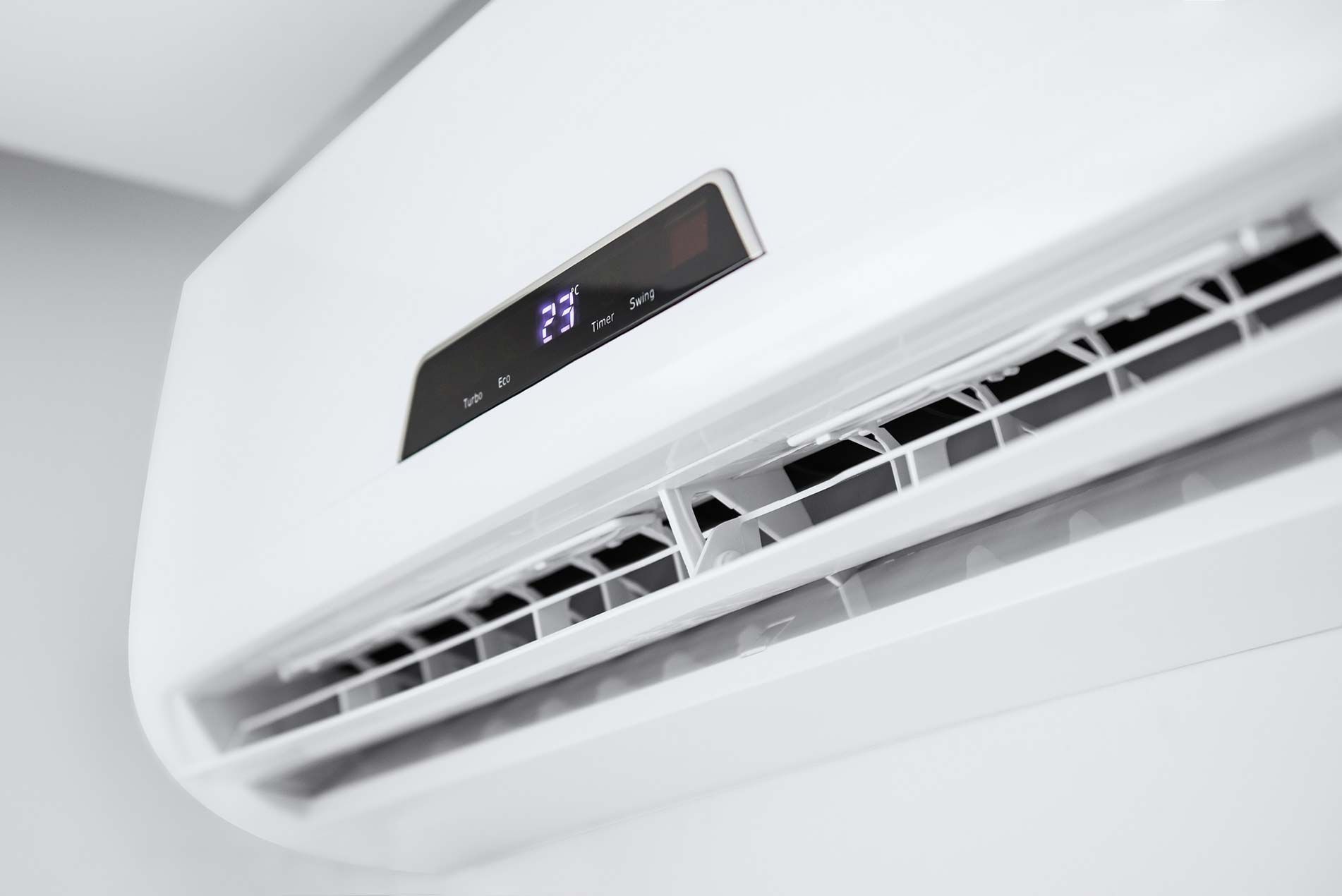 White wall-mounted air conditioner with digital display and open vents in a bright room