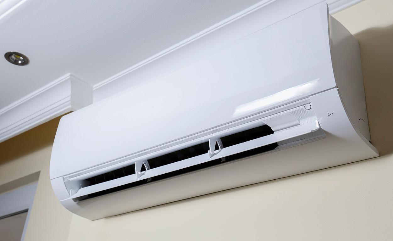 Wall-mounted white air conditioner near the ceiling in a room