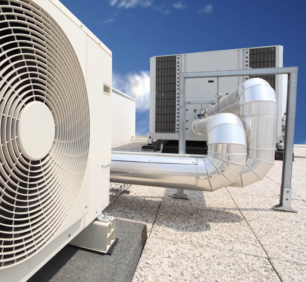 Rooftop HVAC units and large silver ductwork on a flat commercial roof under a blue sky