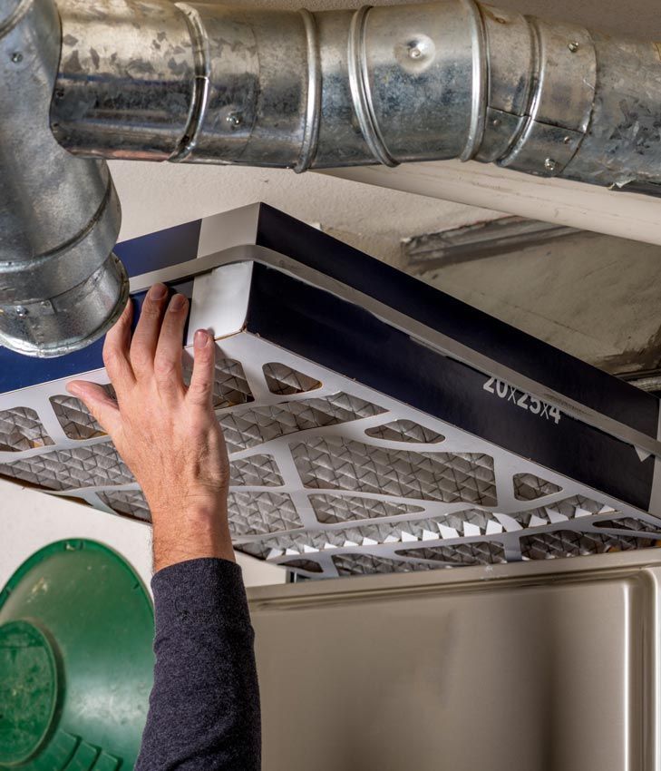 Hand reaching toward a ceiling air vent near exposed metal ductwork