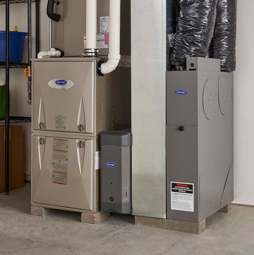 Two gray furnaces and a water heater in a basement utility room.