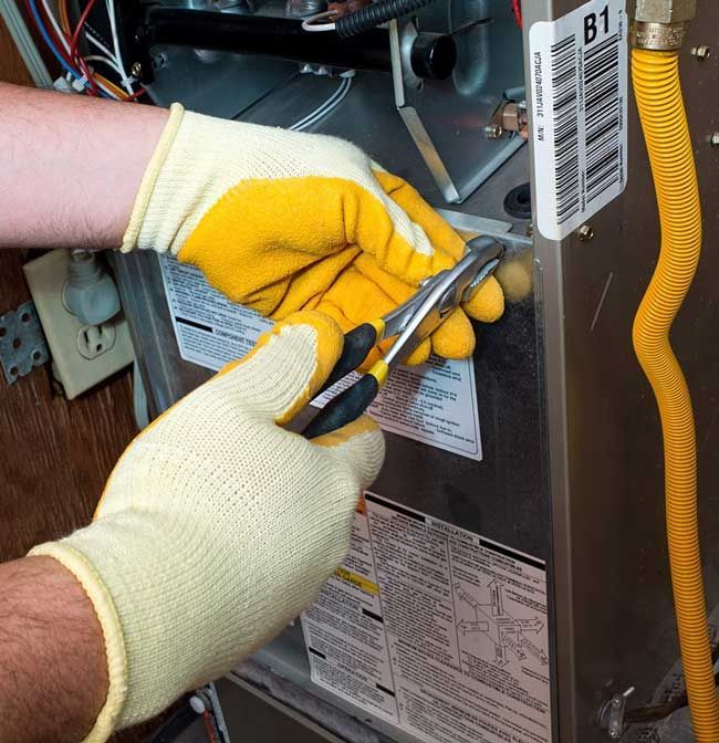 Gloved hands use pliers to cut a wire inside an electrical panel.
