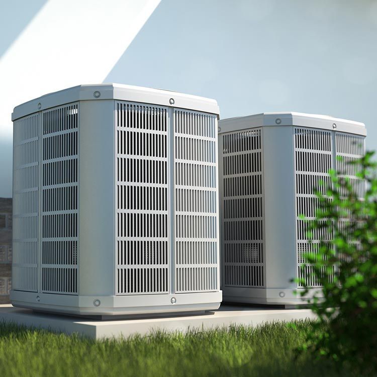 Two white outdoor air conditioning units on grass beside a shrub, under a bright sky