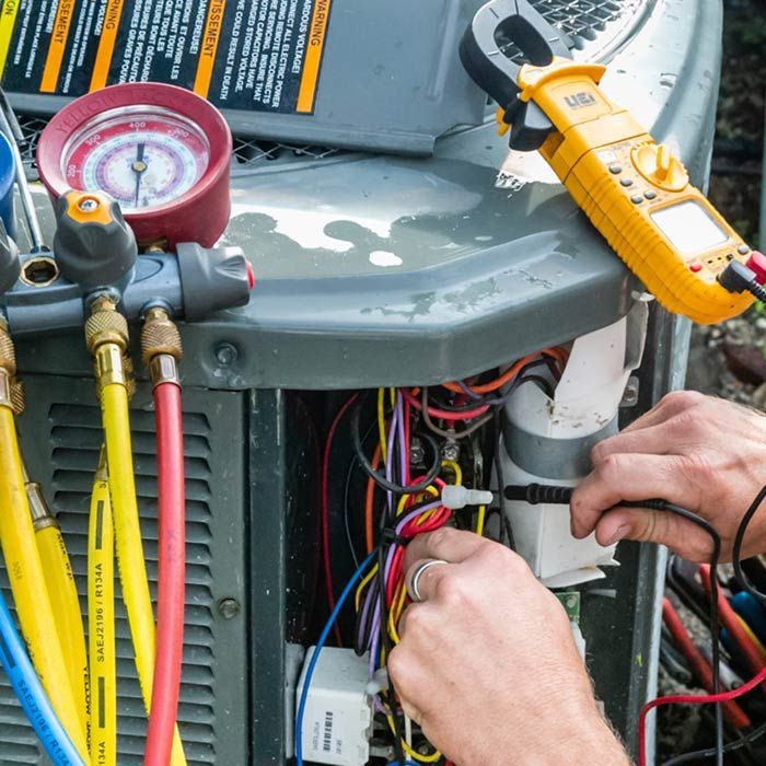 Technician wiring an outdoor HVAC unit with gauges and tools attached