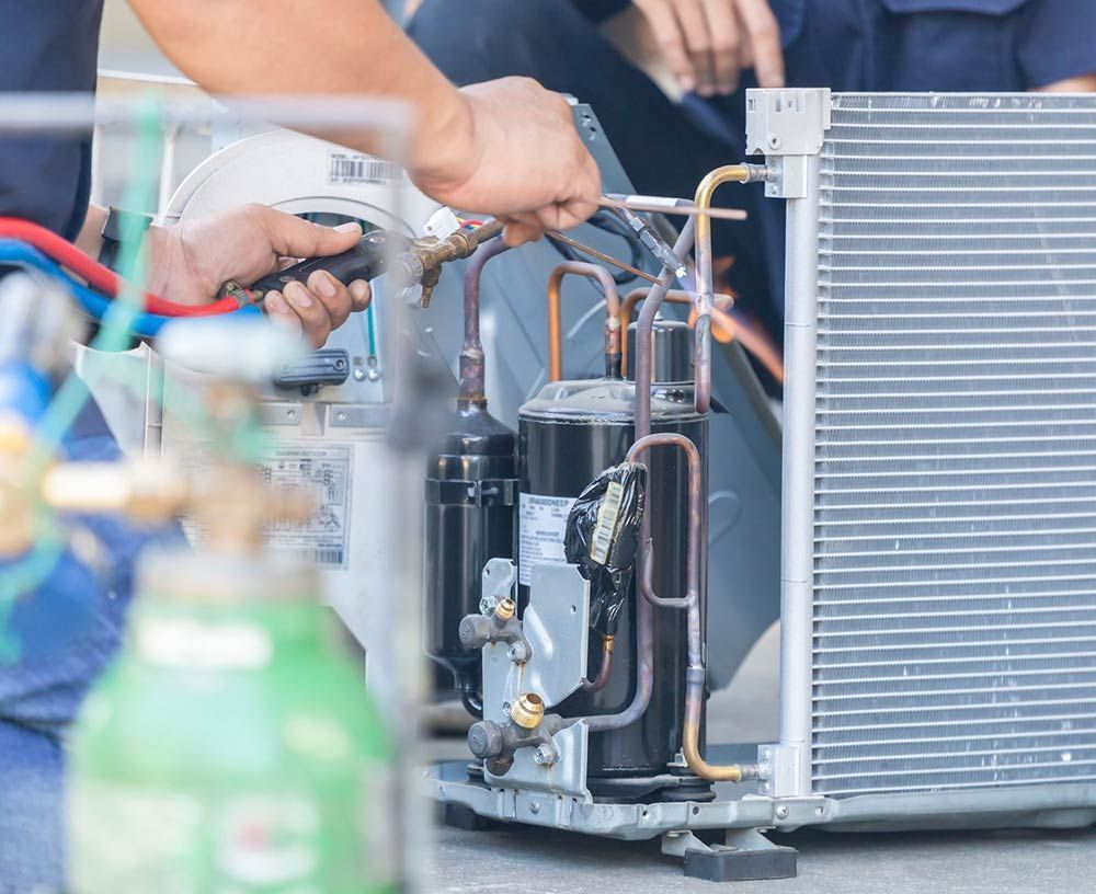 Technician using a heat gun to service an HVAC compressor and radiator unit with copper tubing