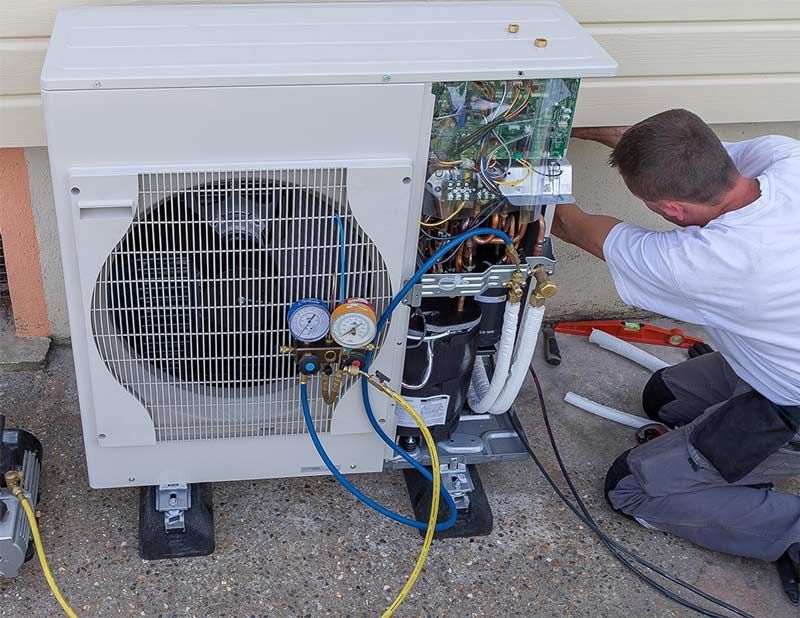 Technician servicing an outdoor air conditioner unit with gauges and exposed wiring