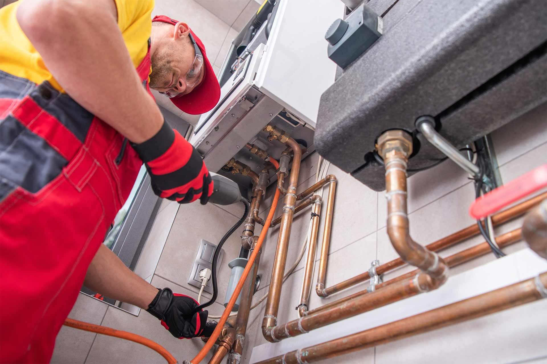 Plumber working on copper pipes inside a utility room, wearing red overalls and gloves.