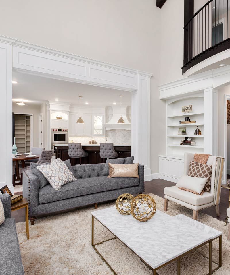 Bright open living room with gray sofa, white armchairs, marble coffee table, and built-in shelves