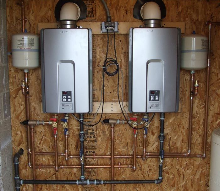 Two wall-mounted tankless water heaters with plumbing and vent pipes in a utility room