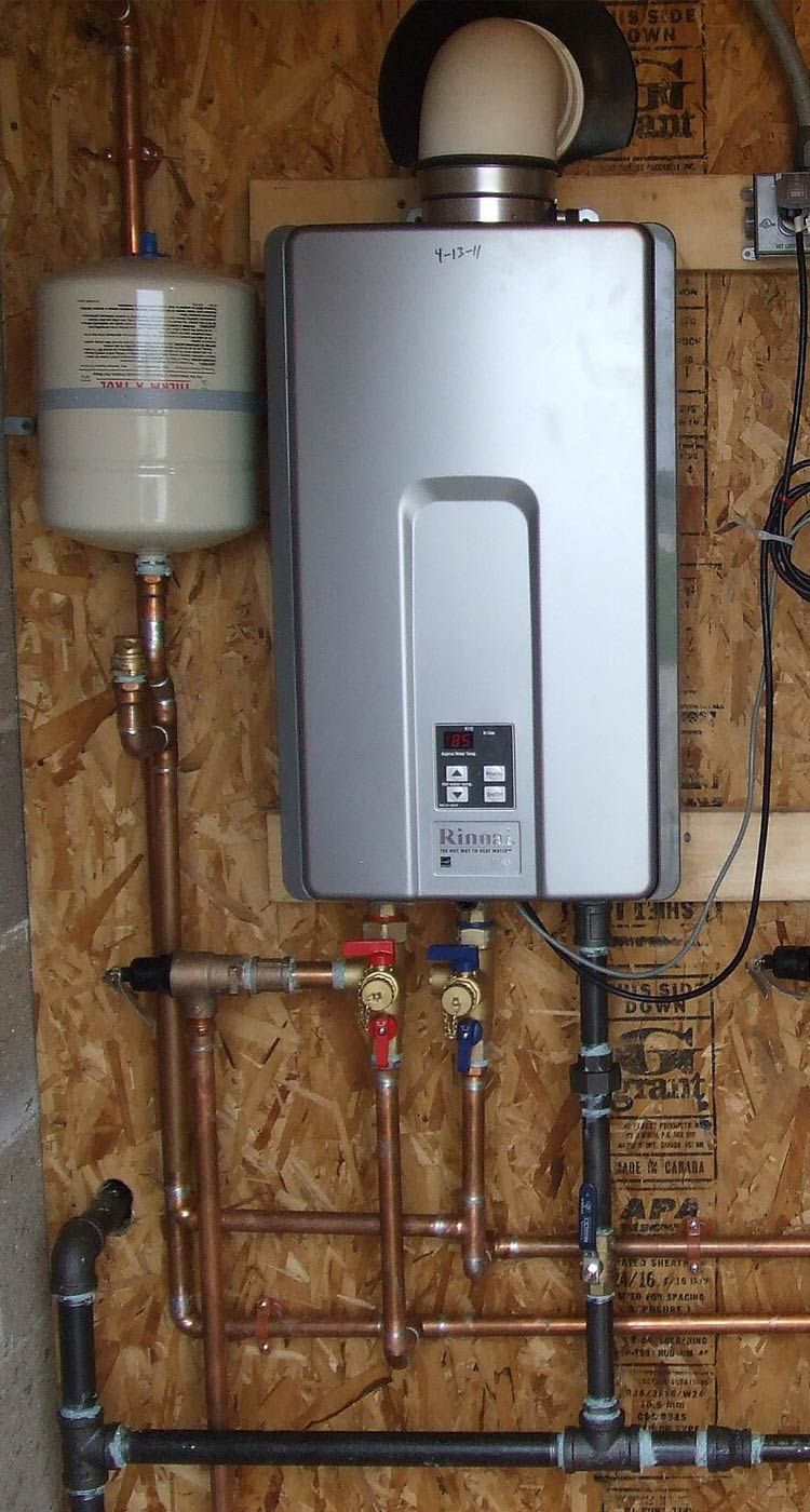 Wall-mounted gas water heater with pipes, valves, and a small expansion tank in a utility area.