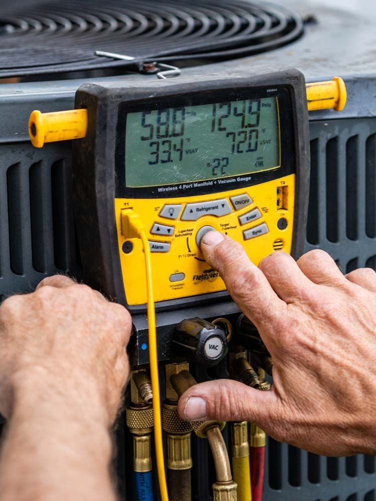 Technician using a yellow HVAC manifold gauge on an outdoor unit to check refrigerant pressure.