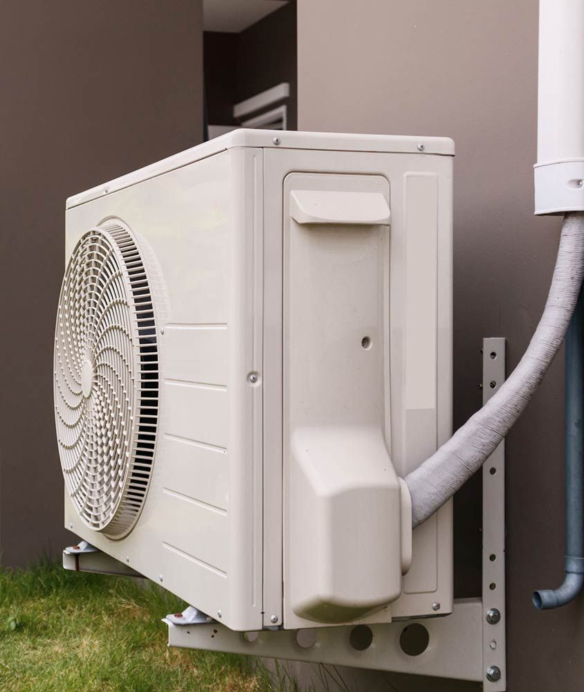 Outdoor wall-mounted air conditioner unit with a large fan and white hose on a building exterior.