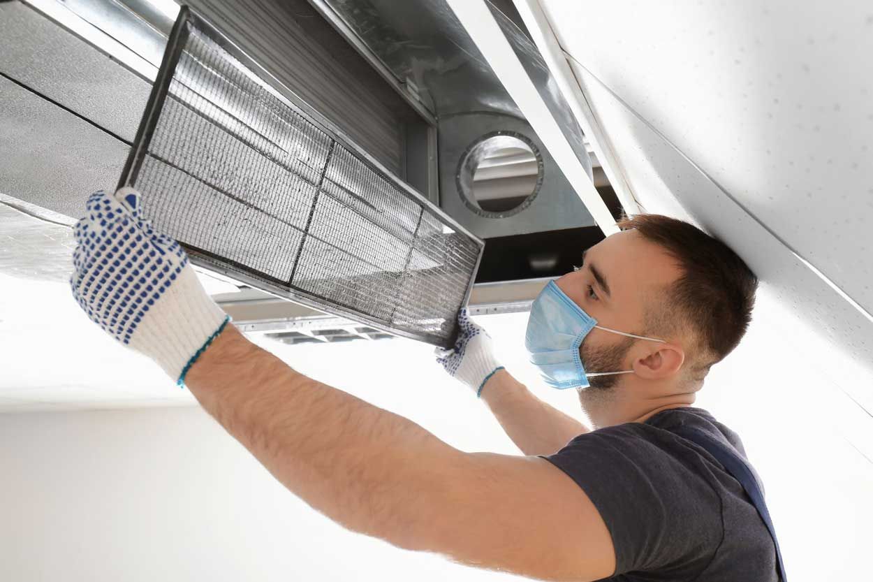 Man in gloves and mask installing a ceiling vent panel indoors