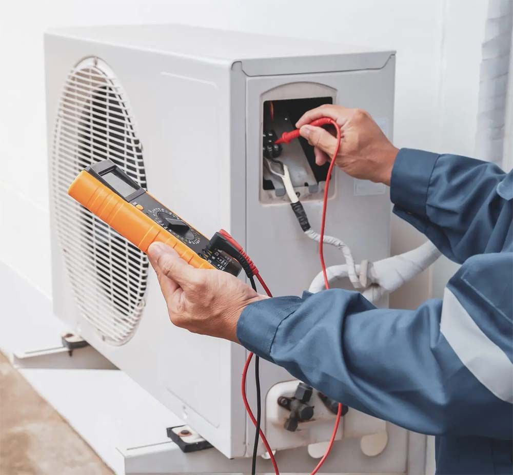 Technician testing an HVAC unit with a multimeter and clamp meter outdoors
