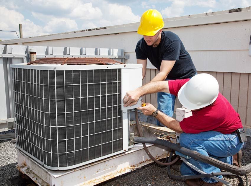 Two workers in hard hats repairing an outdoor air conditioning unit on a rooftop