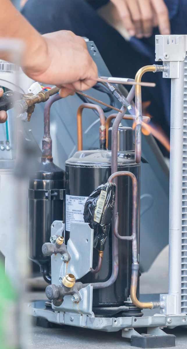 Technician inspecting a copper-piped industrial refrigeration compressor unit.
