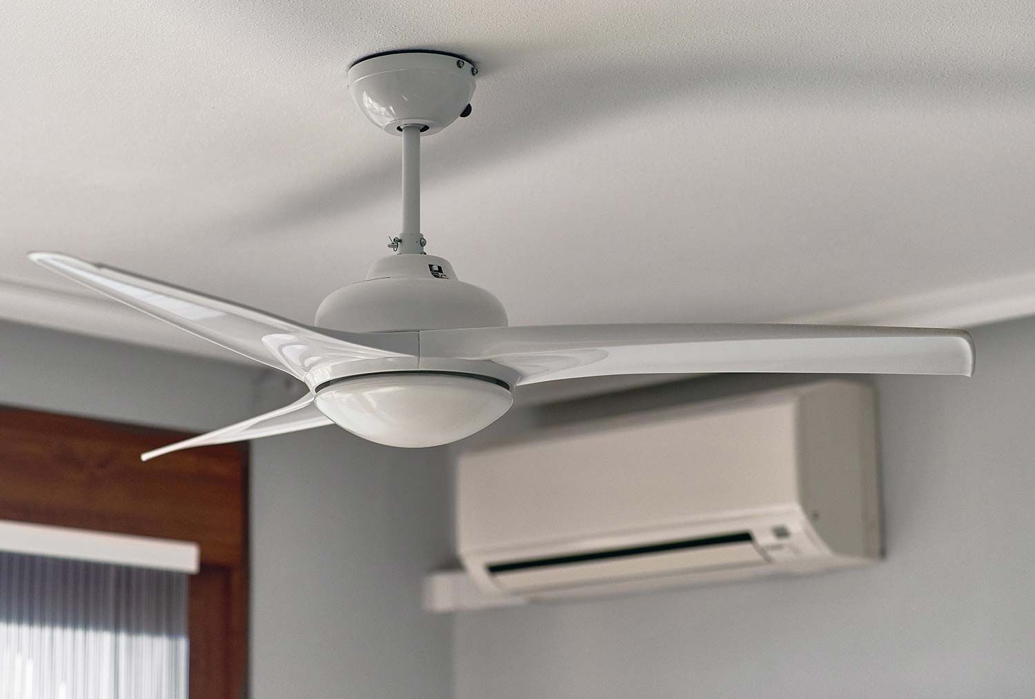 Ceiling fan in a room with a wall-mounted air conditioner above a window