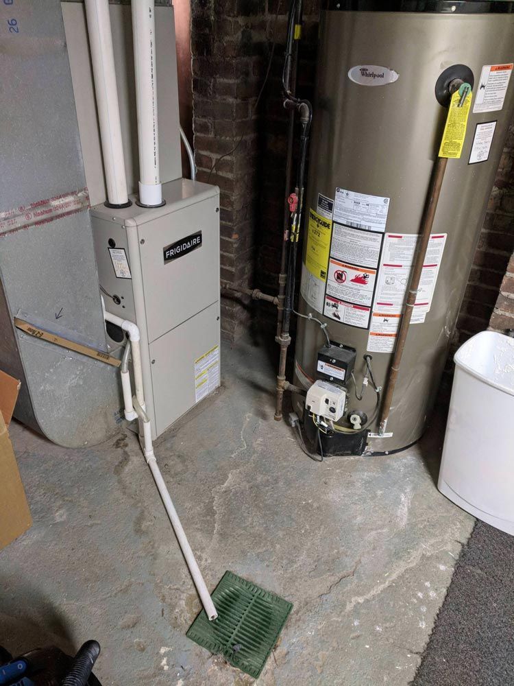 Basement utility area with furnace, water heater, and floor drain by exposed pipes and concrete floor