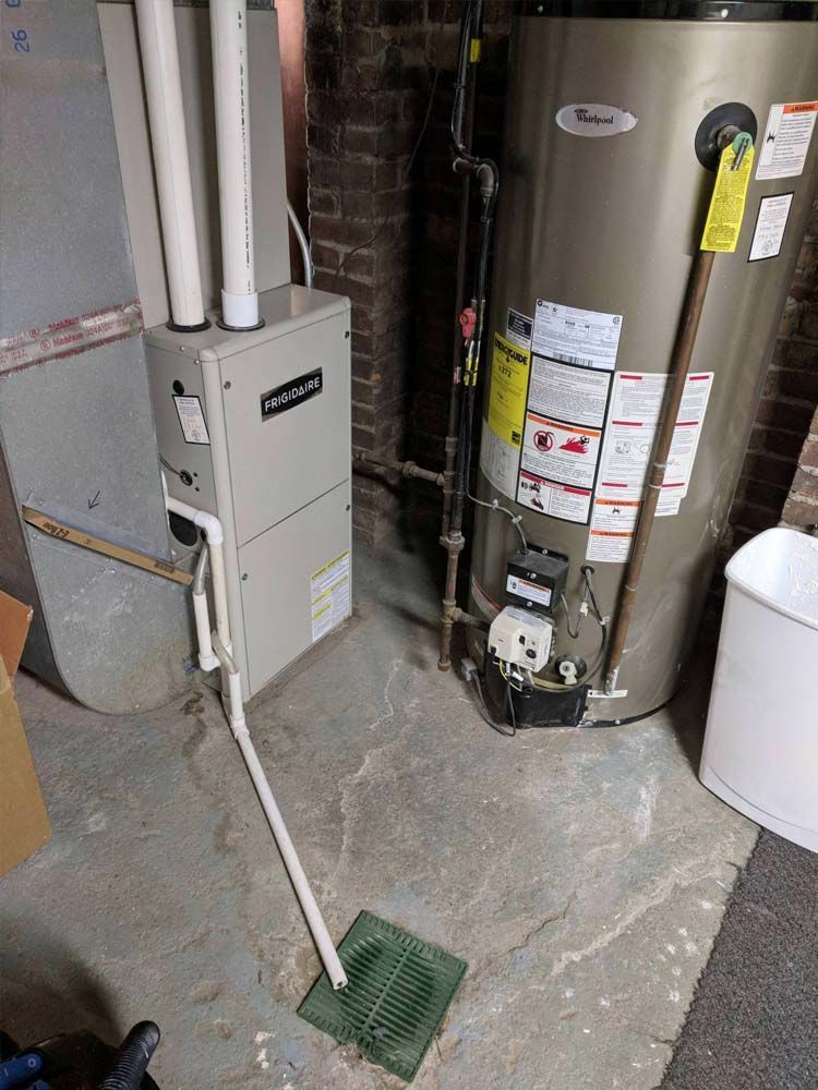 Utility room with water heater, furnace, pipes, and a floor drain in a concrete basement.