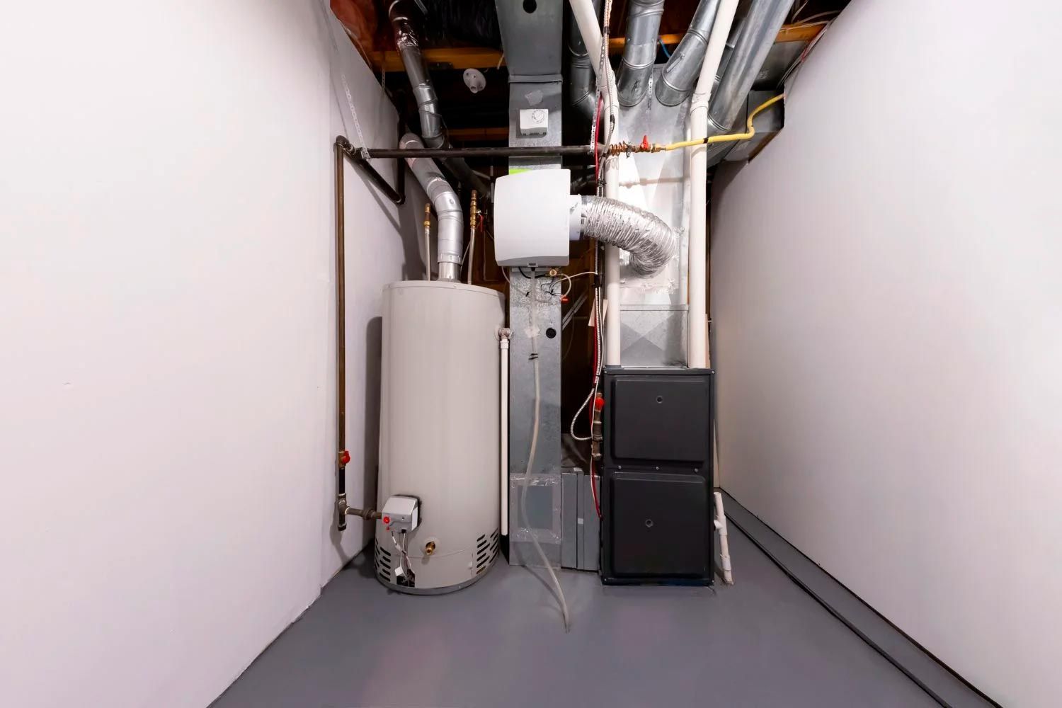 Utility room with water heater, furnace, and exposed pipes in a narrow hallway.