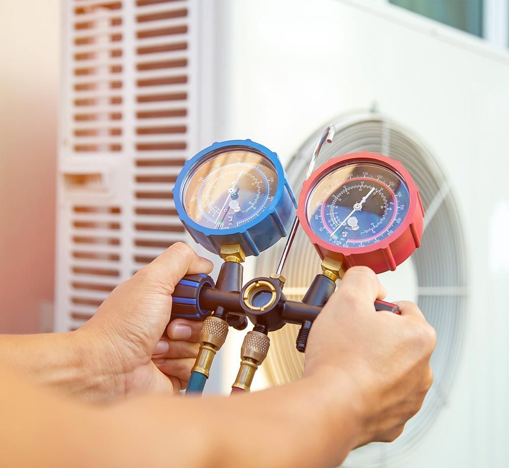 Hands holding blue and red HVAC gauges connected to an air conditioning unit