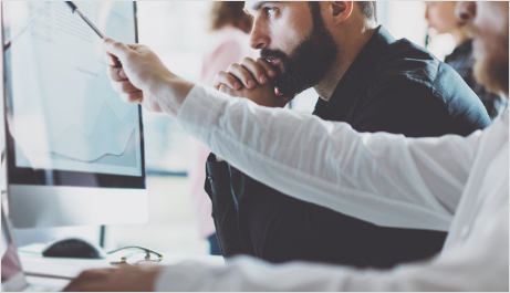 A man with a beard is pointing at a computer screen.